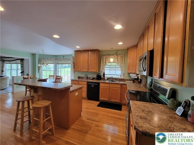 kitchen with appliances with stainless steel finishes, a sink, light wood-style flooring, a kitchen bar, and a kitchen island