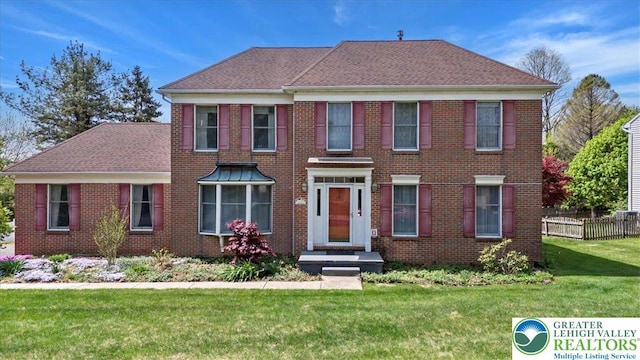 colonial home with brick siding, fence, and a front yard