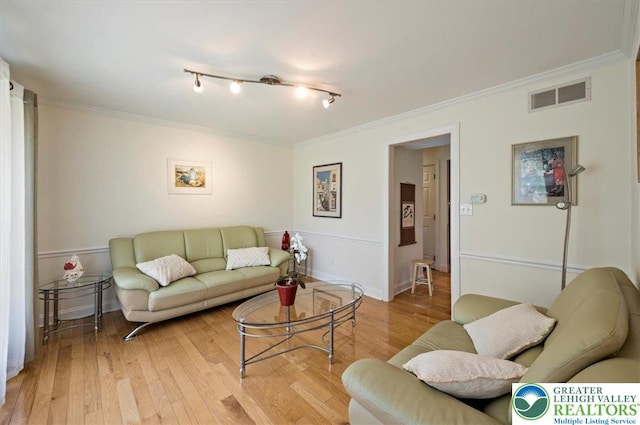 living area with crown molding, light wood finished floors, and visible vents