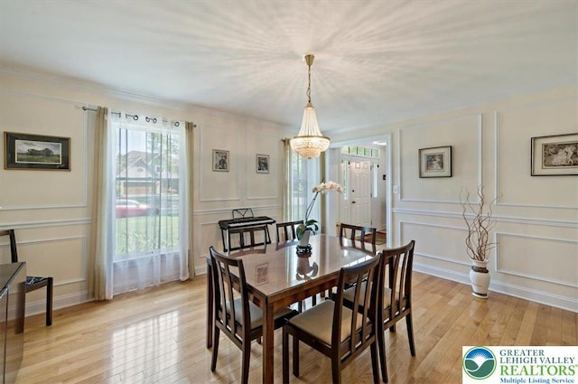 dining room with an inviting chandelier, light wood-style floors, a decorative wall, and ornamental molding