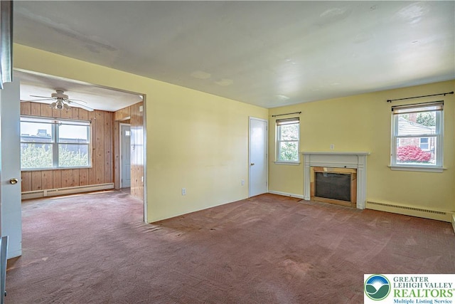 unfurnished living room with baseboard heating, ceiling fan, wood walls, a fireplace with flush hearth, and carpet floors