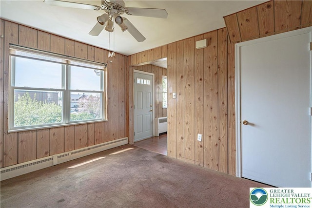 unfurnished room featuring a baseboard heating unit, radiator, wood walls, and carpet