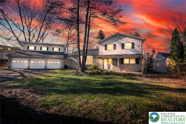 traditional-style home featuring a yard, aphalt driveway, a garage, and brick siding