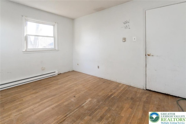 empty room featuring a baseboard heating unit and hardwood / wood-style flooring