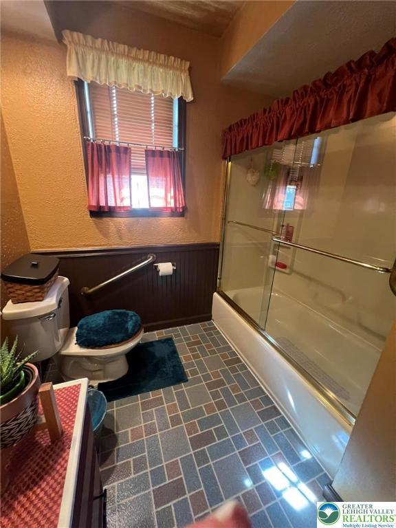 3426 Wilson Ave, South Whitehall Twp, PA 18069 - bathroom featuring wainscoting, toilet, a textured wall, and shower / bath combination with glass door