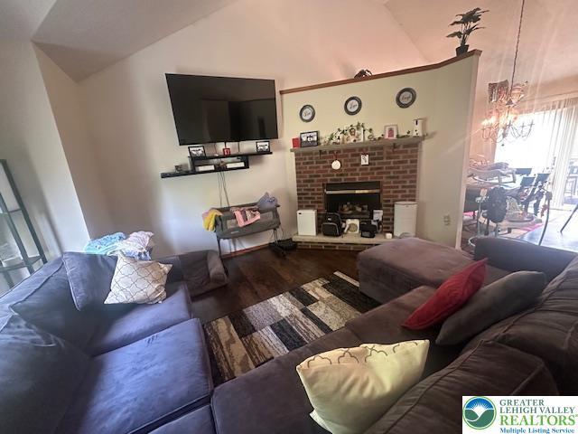 living area with wood finished floors, lofted ceiling, and a brick fireplace