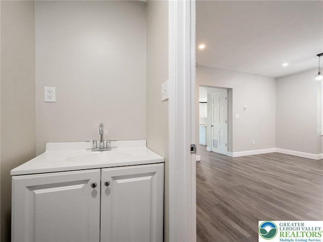 bathroom featuring baseboards, wood finished floors, vanity, and recessed lighting