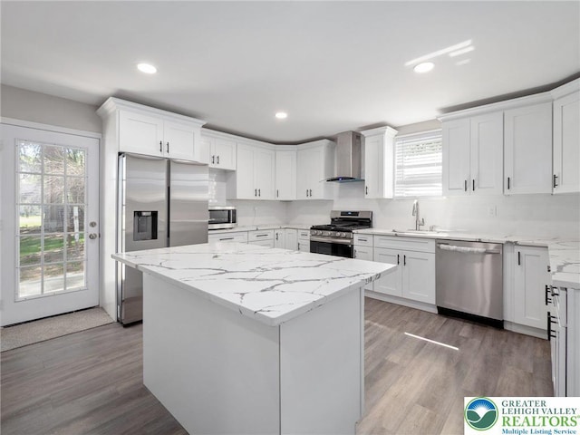 kitchen with stainless steel appliances, white cabinetry, wall chimney range hood, and plenty of natural light