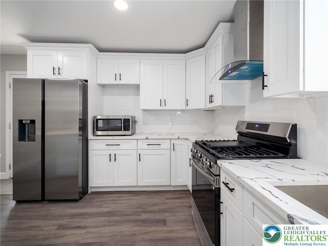 kitchen featuring wall chimney exhaust hood, white cabinetry, light stone countertops, appliances with stainless steel finishes, and decorative backsplash
