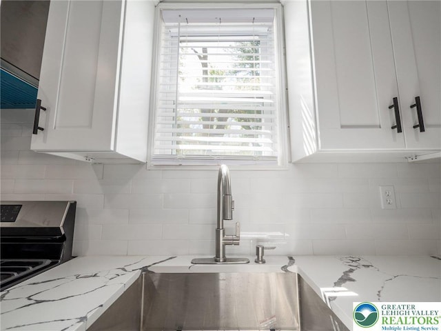 kitchen featuring white cabinetry, light stone counters, a healthy amount of sunlight, and backsplash