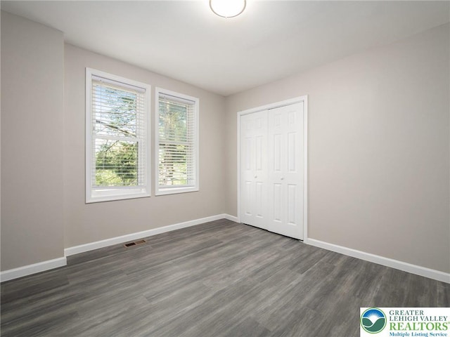 unfurnished bedroom featuring baseboards, dark wood-style floors, visible vents, and a closet