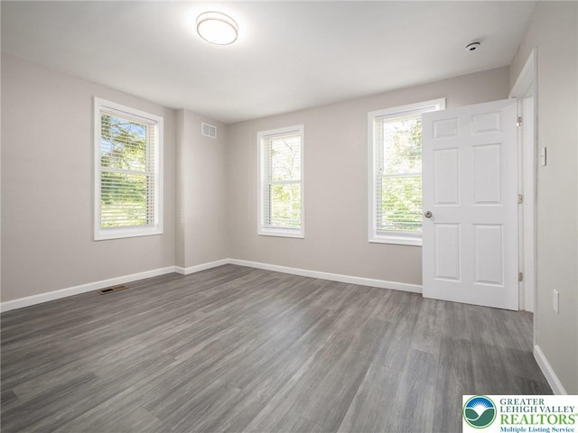 unfurnished room with a wealth of natural light, visible vents, and dark wood-style flooring