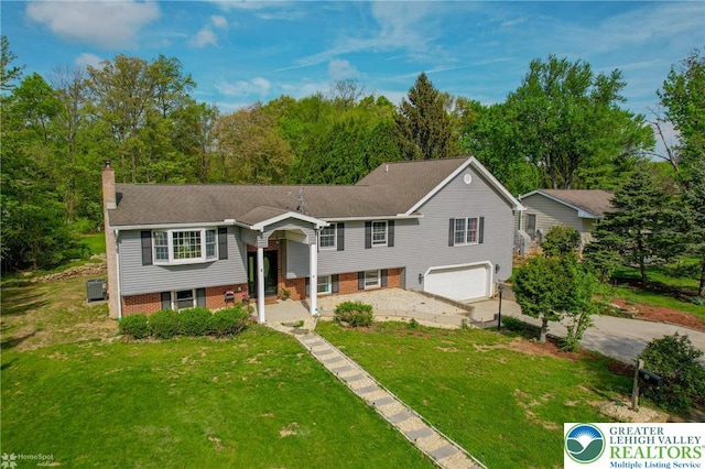 raised ranch with a chimney, driveway, an attached garage, and a front yard