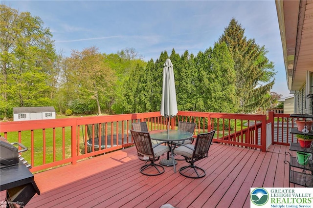 wooden deck featuring a grill, outdoor dining space, an outbuilding, and a lawn