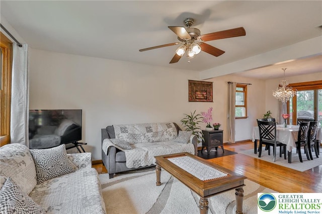 living area featuring ceiling fan with notable chandelier, a wood stove, visible vents, baseboards, and light wood-style floors