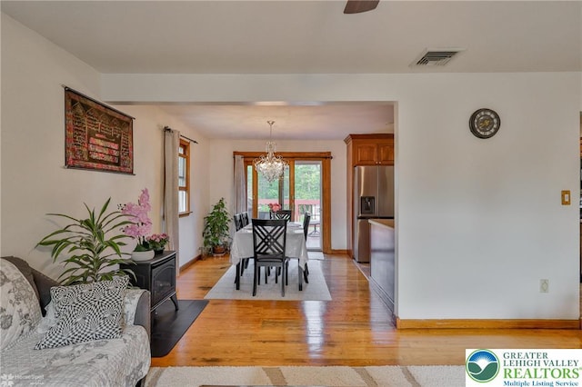 dining area featuring a wood stove, visible vents, a chandelier, light wood finished floors, and baseboards