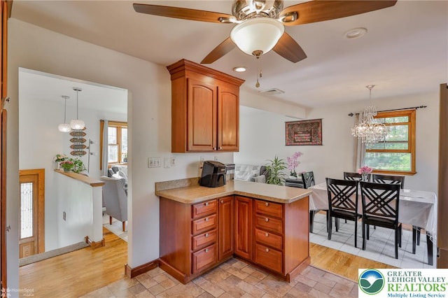 kitchen with a peninsula, light countertops, brown cabinetry, and ceiling fan with notable chandelier