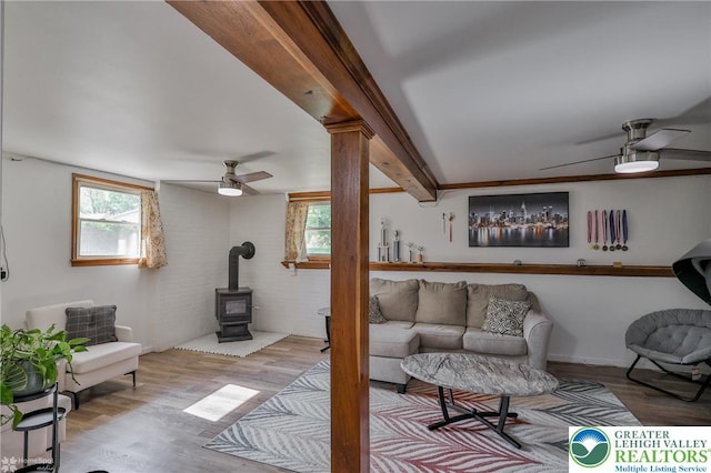 living area with a wealth of natural light, a wood stove, ceiling fan, and wood finished floors