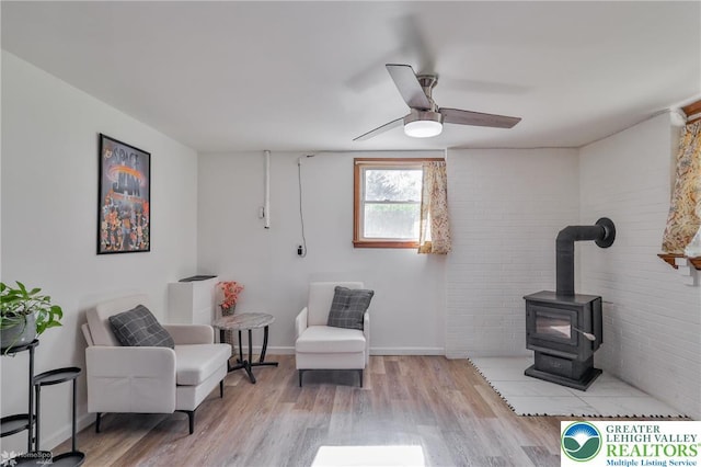 living area with brick wall, ceiling fan, a wood stove, and wood finished floors