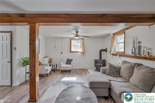 living room featuring a wood stove, ceiling fan, beamed ceiling, baseboards, and light wood-style floors