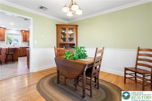 dining room featuring ornamental molding, visible vents, a chandelier, light wood finished floors, and wainscoting
