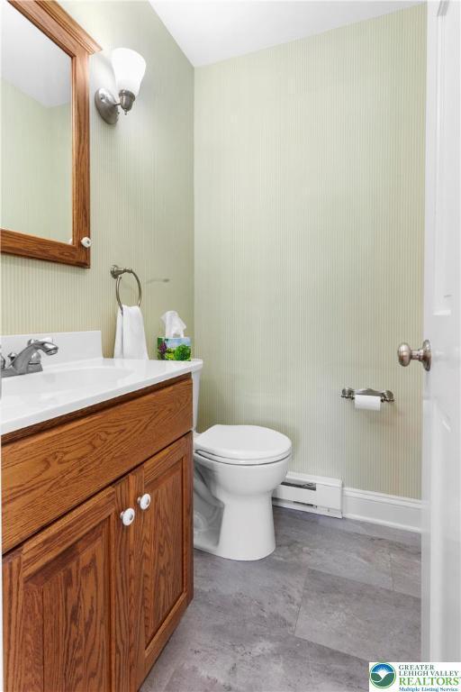 half bathroom with a baseboard heating unit, vanity, and toilet
