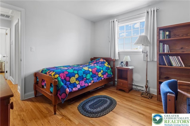 bedroom with baseboards, visible vents, and wood finished floors