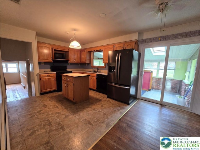 kitchen with a center island, a sink, pendant lighting, black appliances, and light countertops