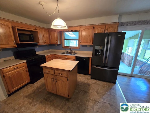 kitchen with a sink, black appliances, light countertops, hanging light fixtures, and a kitchen island