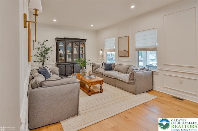 living room with wood finished floors, visible vents, a decorative wall, and recessed lighting