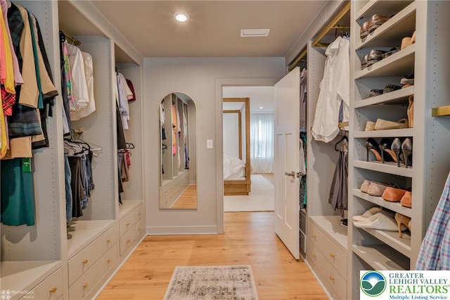 walk in closet featuring light wood-style flooring, arched walkways, and visible vents