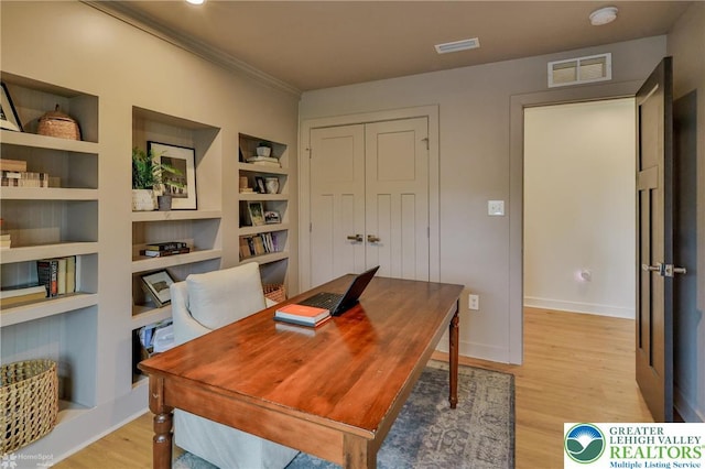 office space with light wood-type flooring, ornamental molding, visible vents, and built in features