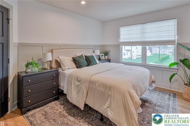 bedroom featuring a decorative wall, wood finished floors, wainscoting, and recessed lighting