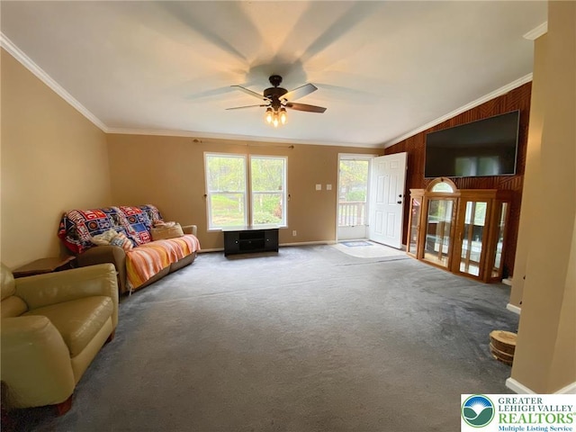carpeted living room featuring crown molding, ceiling fan, baseboards, and wood walls