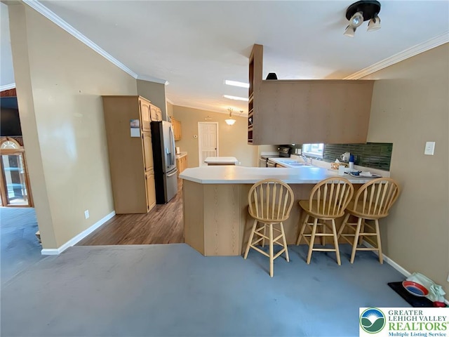 kitchen with stainless steel refrigerator with ice dispenser, ornamental molding, baseboards, a kitchen bar, and a peninsula