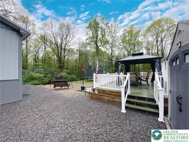 wooden deck with a trampoline, a gazebo, and view of wooded area