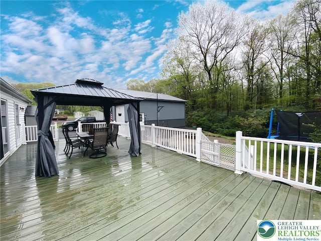 deck with outdoor dining area, a trampoline, and a gazebo