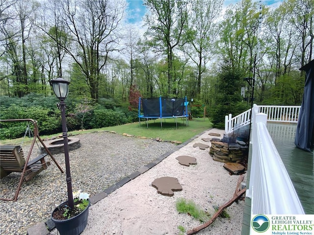 view of yard featuring an outdoor fire pit, a trampoline, and a deck