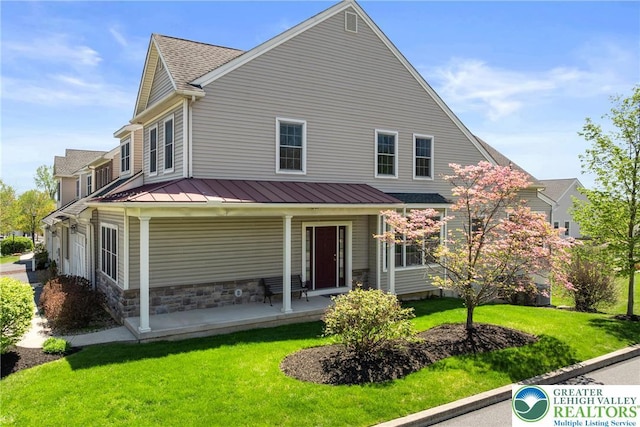 farmhouse-style home featuring covered porch, a front lawn, a standing seam roof, and metal roof