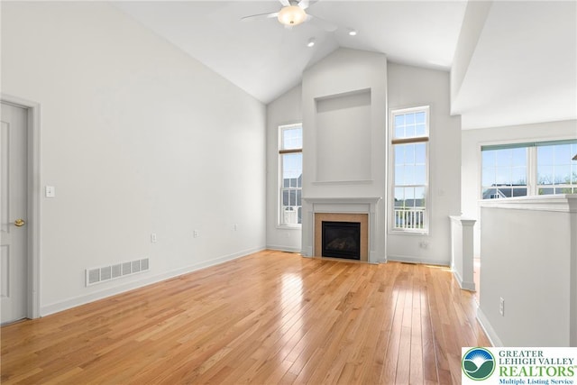unfurnished living room with high vaulted ceiling, a ceiling fan, light wood-style floors, a glass covered fireplace, and baseboards