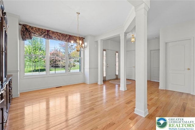 unfurnished dining area with decorative columns, light wood-type flooring, a chandelier, and baseboards