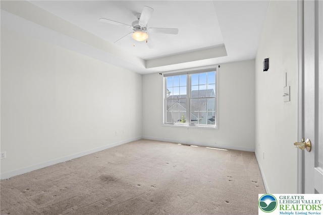 carpeted spare room featuring a tray ceiling, a ceiling fan, and baseboards