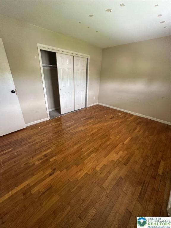 unfurnished bedroom featuring wood finished floors, baseboards, and a closet