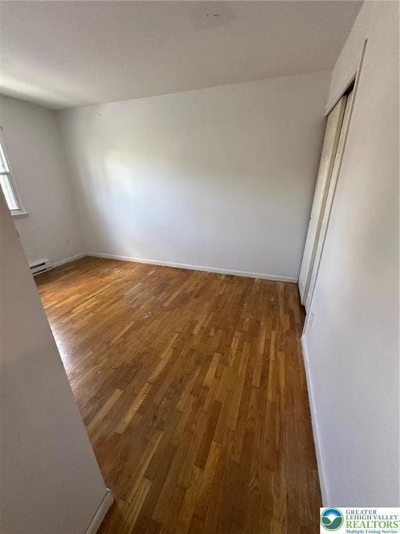 unfurnished bedroom with wood finished floors, baseboard heating, and baseboards