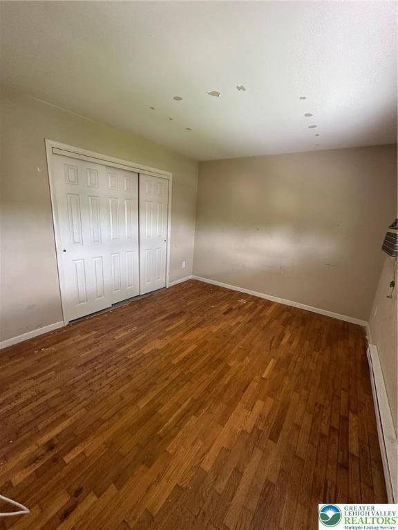 unfurnished bedroom with wood finished floors, baseboards, and baseboard heating
