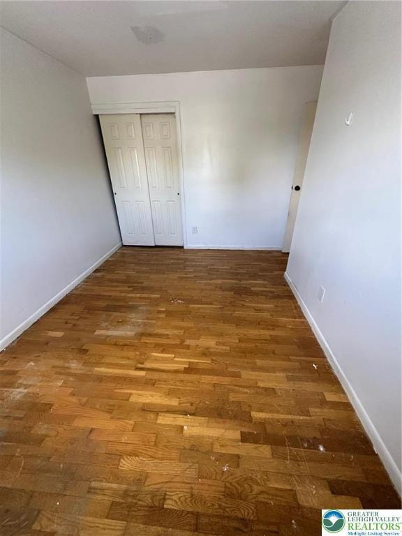 unfurnished bedroom with wood finished floors, baseboards, and a closet