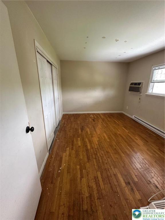 unfurnished bedroom with a wall mounted AC, hardwood / wood-style flooring, and baseboards