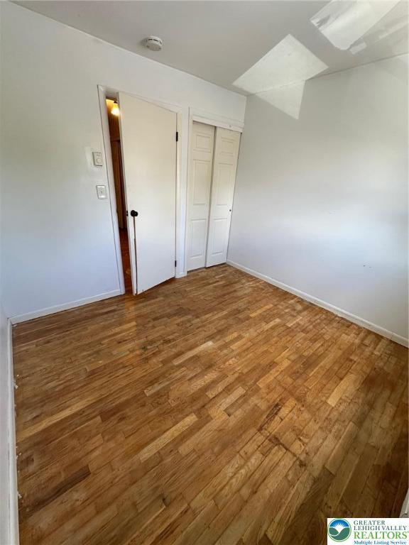 unfurnished bedroom featuring baseboards, wood finished floors, and a closet