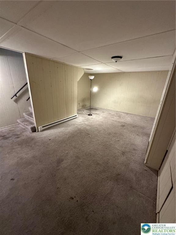 finished basement featuring carpet flooring, baseboard heating, wood walls, and stairs