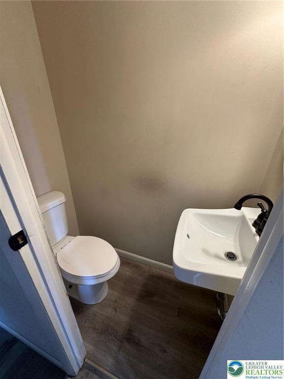 half bath with wood finished floors, toilet, a sink, and baseboards